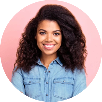 A woman in a blue denim shirt smiles while standing in front of a pink background.