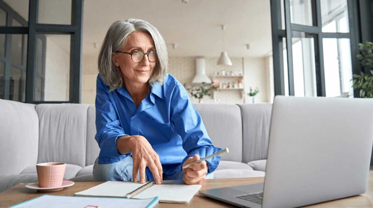 Woman takes notes in front of laptop while she works on growing her solo business through email.