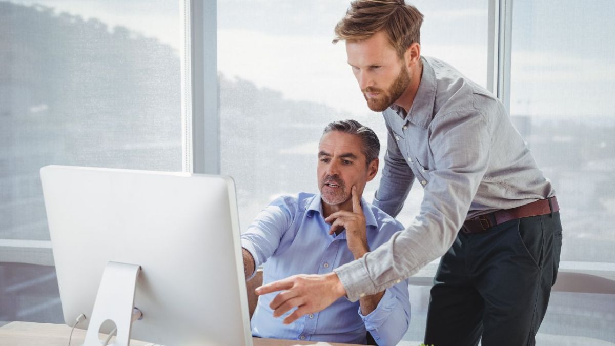 Two middle-aged men look at a computer to find their email bounced and wonder how they could have avoided it from bouncing.