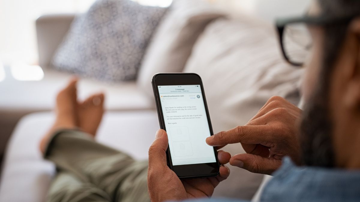 Barefoot, bespectacled man lounges on the couch confident that he's ended his email effectively.