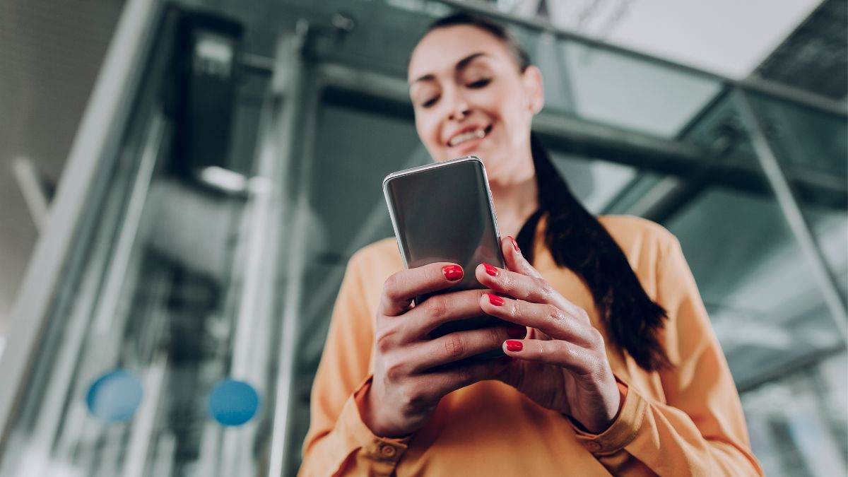 Young woman with brightly painted nails holds mobile phone to send quick follow-up email.