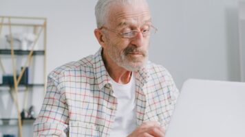 Bespectacled senior citizen man sits before his computer and changes his Gmail sender name.