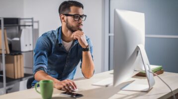 Bespectacled and bearded man sits at his email preparing to reach out to another business owner.