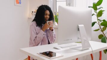 Young woman holds mug with hot beverage while planning to write a professional email.