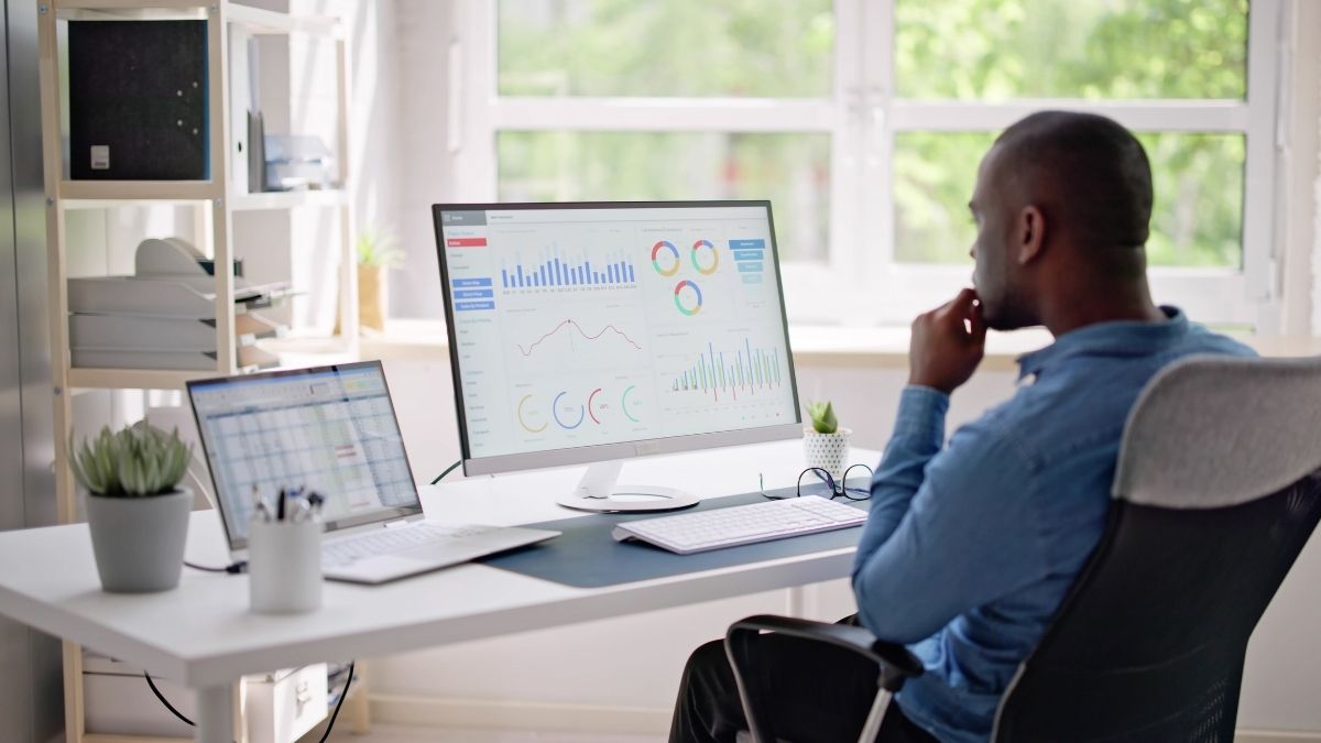 African American man sits at his desktop and laptop in order to test email deliverability.