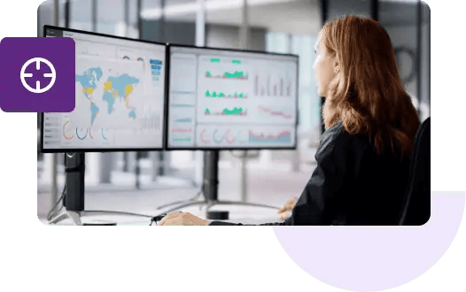 A shot of a woman from behind looking at two monitors that feature geolocation maps and various graphs.