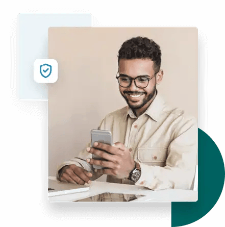 Man sitting at a desk smiling while using ZeroBounce's email validation on his mobile phone.