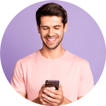Un hombre con una camisa rosa sostiene y mira su teléfono inteligente y sonríe