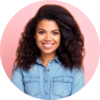 A woman wearing denim smiles at the camera in front of a pink background.