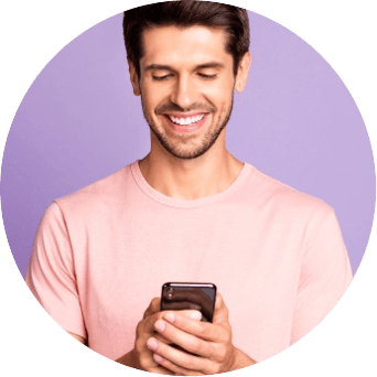 Un hombre sonriente con una camisa rosa mira su teléfono móvil.