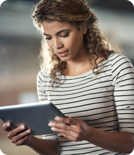 A woman in a white shirt with black stripes looks at a tablet and a rising bar graph titled ‘Revenue.’