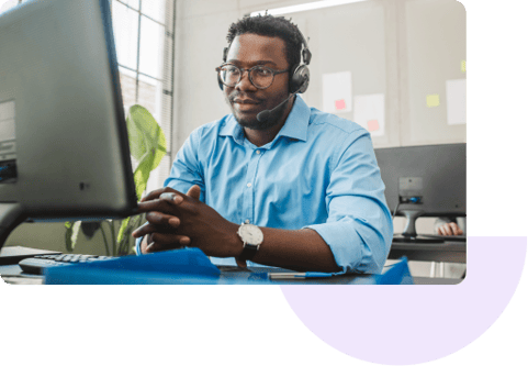 A customer service agent wearing a headset talks to a customer in front of his computer.