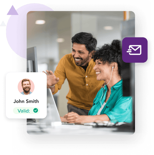 A woman seated at her desk and a man standing next to her smile while looking at a computer screen alongside a profile for ‘John Smith’ with a ‘Valid’ message.