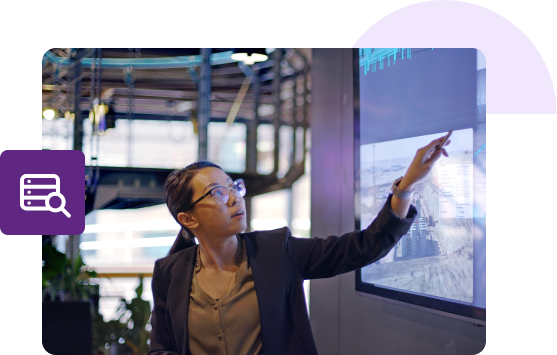 A woman in a blazer looks and points to an item on a projection screen.