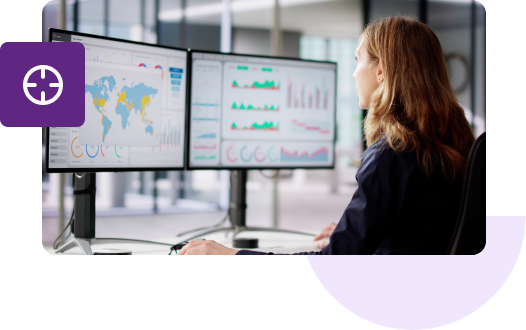 A shot of a woman from behind looking at two monitors that feature geolocation maps and various graphs.