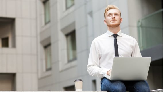 Redheaded man sits down at his laptop outside wondering if he can check email addresses without sending an email.