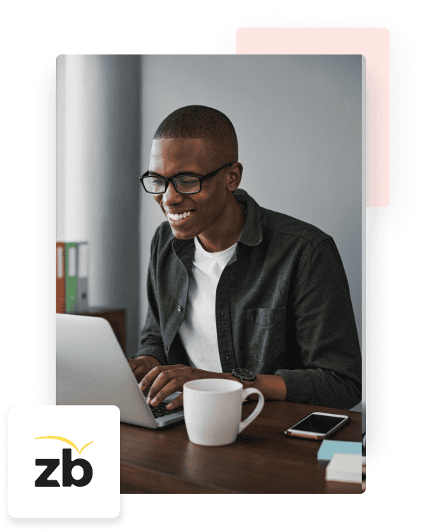 A man wearing a white shirt and green button-down smiles while seated at his desk in front of his laptop, a white mug, and the ZeroBounce BIMI logo.